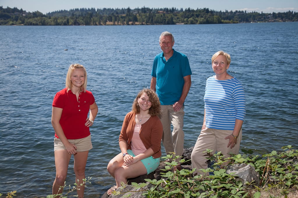 Family photo of couple with their two grown daughters, posed on the waterfront along Lake Washington